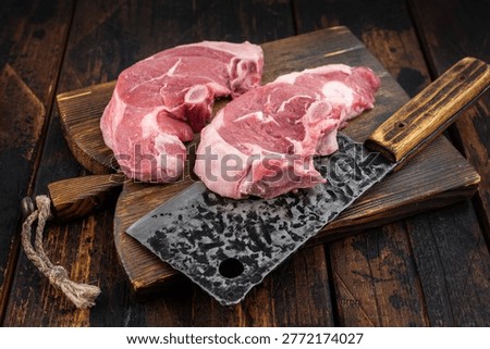 Raw lamb chump chops with bone on rustic wooden board, fresh sirloin saddle cuts near butcher cleaver, premium red meat prepared for roasting or grilling recipes