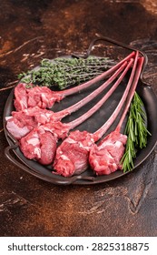 Raw lamb cutlets on bone in cast iron skillet with herbs warm dark background top view butcher meat copy space.