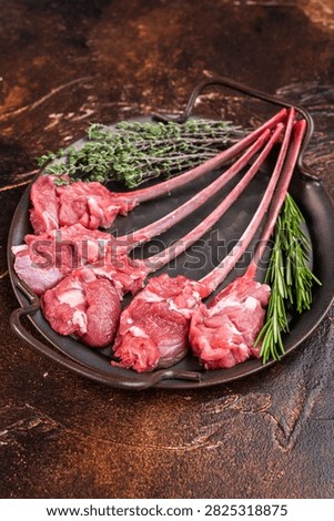 Raw lamb cutlets on bone in cast iron skillet with herbs warm dark background top view butcher meat copy space.