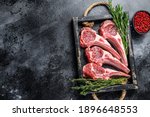Raw lamb meat chops steaks in a wooden tray. Black background. Top view. Copy space.