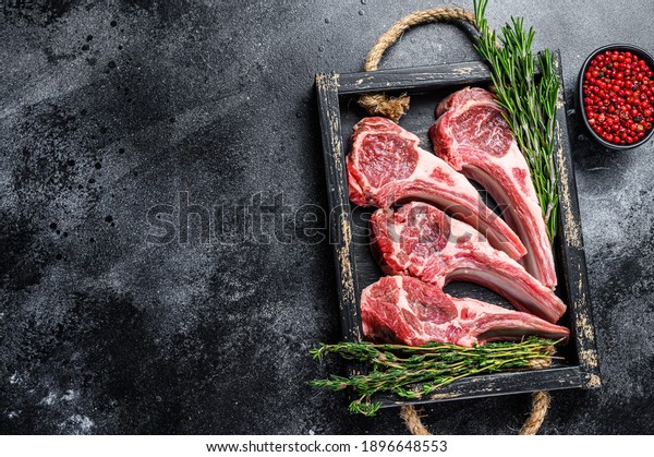 Raw lamb meat chops steaks in a wooden\
tray. Black background. Top view. Copy\
space.