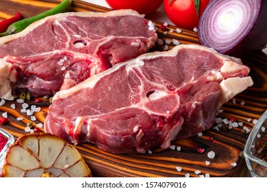 Raw lamb meat on a wooden cutting board with spices and fresh vegetables