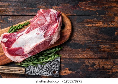 Raw lamb mutton shoulder meat on the bone on a wooden butcher cutting board with cleaver. Dark wooden background. Top view. Copy space.
