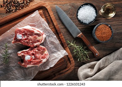 Raw Lamb Neck Meat On White Cooking Paper And Wooden Cutting Board. Decorated With Herbs, Spices, Chef's Knife And Napkin. Overhead View.