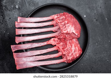 Raw lamb rack ribs with bone on cast iron skillet dark stone background top view butcher meat with copy space.
