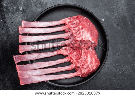 Raw lamb rack ribs with bone on cast iron skillet dark stone background top view butcher meat with copy space.