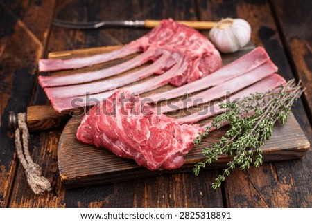 Raw lamb rack ribs with bone on rustic wooden board dark background top view butcher style meat with copy space.