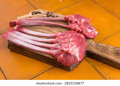 Raw lamb rack ribs and chops steaks on wooden board terracotta tile background top view butcher meat with copy space.