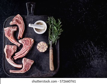 Raw Lamb Ribs on a rustic metal board with rosemary, garlic salt and pepper. Black Background. Top View