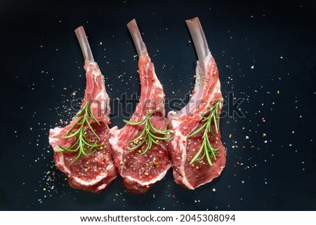 raw lamb saddle meat on bone with salt, pepper decorated rosemary top view on black background