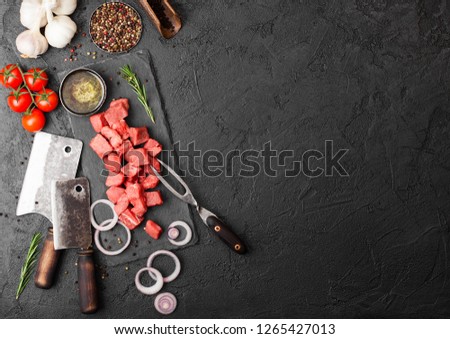 Raw lean diced casserole beef pork steak with vintage meat hatchet and fork on stone background. Salt and pepper with fresh rosemary, red onion and garlic.