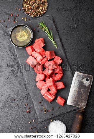 Raw lean diced casserole beef pork steak on chopping board with vintage meat hatchet on stone background. Salt and pepper