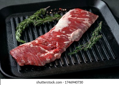 Raw machete steak on beef in a grill pan with seasoning. Stone background.
