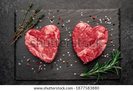 raw marbled beef steaks in the shape of a heart with spices on a stone background