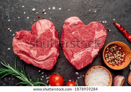raw marbled beef steaks in the shape of a heart with spices on a stone background

