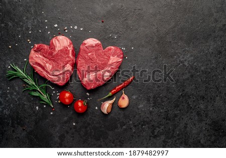 raw marbled beef steaks in the shape of a heart with spices on a stone background copy of the space for your text