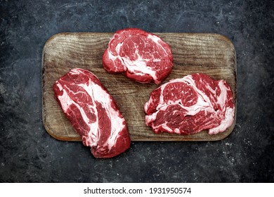 Raw Marbled Sirloin Beef Steaks On Wooden Cutting Board. Sirloin Beef Steaks, Overhead View. Many Raw Striploin Steaks From Marbled Beef On Black Background, Top View.