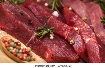 Raw meat. Raw beef steak on a cutting board with rosemary and spices on wooden background. - Powered by Shutterstock