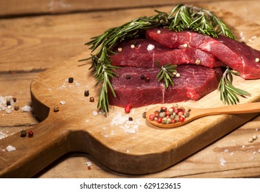 Raw meat. Raw beef steak on a cutting board with rosemary and spices on wooden background. - Powered by Shutterstock