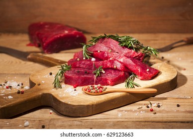 Raw meat. Raw beef steak on a cutting board with rosemary and spices on wooden background. - Powered by Shutterstock