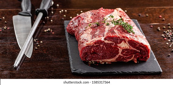 Raw meat. Beef tenderloin, neck lies on a black board, next to a knife and knife sharpener. closeup. background image. copy space