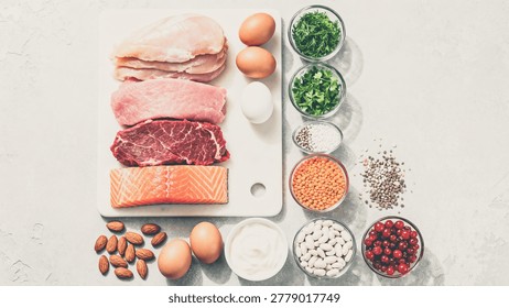 Raw meat, eggs, nuts, and various healthy food ingredients arranged on a white cutting board and surrounding surface, showcasing a selection of protein-rich foods and fresh produce in a clean and orga