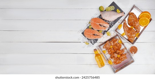 Raw meat and fish arranged on a white table, featuring a red fish steak, sea bass carcass, marinated chicken breast, and duck shank. Top view