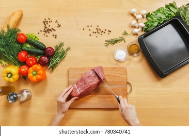 Raw Meat. Fresh Beef Tenderloin On Cutting Board On Wooden Table With Different Vegetables, Spices, Mushrooms, Baking Tray, Knife. Top View Flatlay. Copy Space . Woman Cuts With Knife