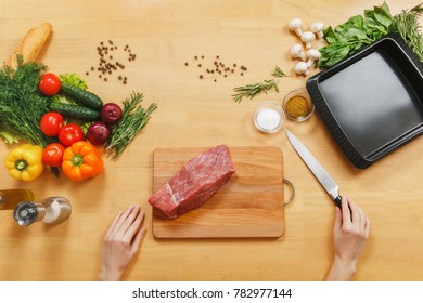 Raw Meat. Fresh Beef Tenderloin On Cutting Board On Wooden Table With Different Vegetables, Spices, Mushrooms, Baking Tray, Knife. Top View Flatlay. Copy Space . Woman Cuts With Knife