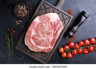 Raw meat. Japanese marble beef. Wagyu. Rib eye steak on a black wooden board on a black table with spices, thyme, cherry tomatoes. Background image, copy space, flatlay, top view - Shutterstock ID 2095497493
