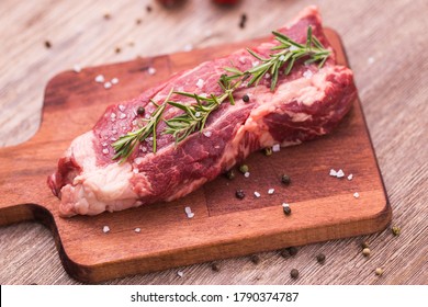 Raw meat. A large piece of beef chop on a wooden cutting board with rosemary and spices.