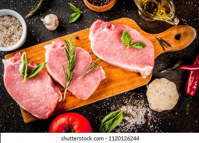 Raw meat, pork steaks with spices, herbs, olive oil, dark background top view, copy space