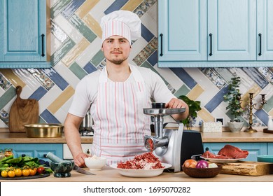 Raw meat. The process of preparing minced meat is carried out using a meat grinder. A male chef uses a meat grinder in the kitchen - Powered by Shutterstock