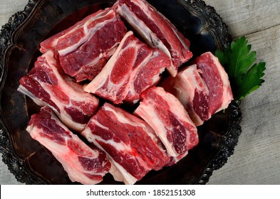 Raw Meat Ribs On A Black Silver Plate, Gray Wooden Background. Raw Organic Beef Short Ribs
