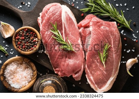 Raw meat steaks with spices, herbs and oil at dark background.