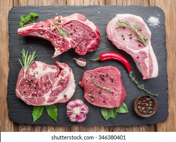 Raw meat steaks with spices on the black cutting board.