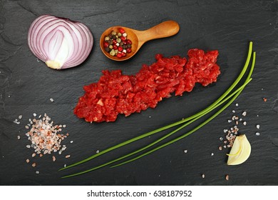 Raw minced beef red meat cutlet, spices, peppercorns, spring shallot onions, garlic and salt on black slate board, close up, elevated top view, directly above - Powered by Shutterstock