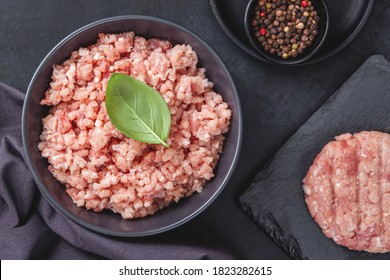 Raw minced meat in bowl on black stone table and ingredients. Ground meat with ingredients for cooking on dark background with copy space. Top view or flat lay