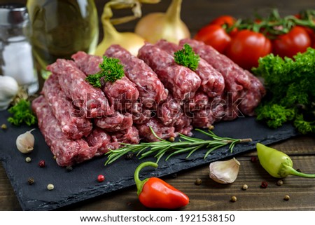 Raw minced meat cevapi ready for barbeque with various fresh vegetables on a wooden table. Selective focus.