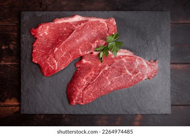 Raw minute steak of marbled beef with a parsley leaf on a stone slate board, flat lay, top view - Shutterstock ID 2264974485