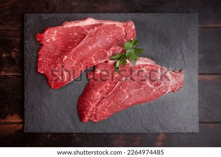 Raw minute steak of marbled beef with a parsley leaf on a stone slate board, flat lay, top view