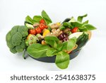 Raw mixed organic vegetables arranged in a dark bowl, on a white background. Includes broccoli, Pac Choi, red onion, garlic, Brussels sprouts, tomatoes, bell peppers, mushrooms ect.