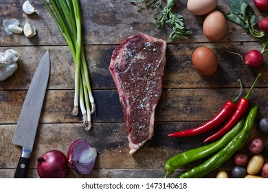 Raw New York Strip Steak With Farm Fresh Eggs Potatoes And Vegetables On Wooden Table With Knife