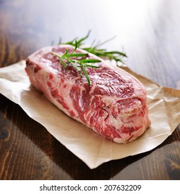 Raw New York Strip Steak On Brown Parchment Paper With Rosemary