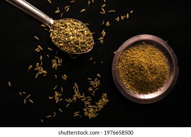 Raw Organic Fennel Seeds Placed On A Steel Spoon Along With Fennel Seed Powder Placed On A Steel Plate Against A Black Background