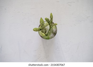 Raw Organic Green Asparagus In Glass Viewed From Above On White Wood Background, Top View, Copy Space. Plant Based Food