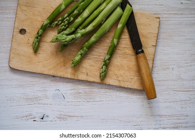 Raw organic green asparagus ready to cook on cutting board on white wood background, top view, copy space. Plant based food