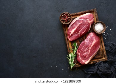 Raw organic marbled beef steaks with spices  on a wooden cutting board on a  black slate, stone or concrete background. Top view with copy space. - Shutterstock ID 1921889300