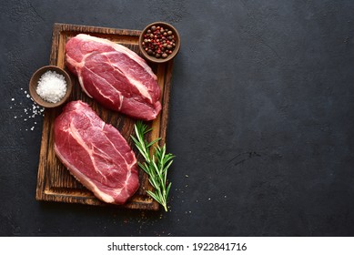 Raw organic marbled beef steaks with spices  on a wooden cutting board on a  black slate, stone or concrete background. Top view with copy space. - Shutterstock ID 1922841716