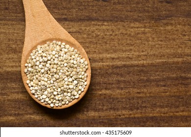 Raw Organic White Quinoa (lat. Chenopodium Quinoa) Grains On Small Wooden Spoon, Photographed Overhead On Dark Wood With Natural Light

